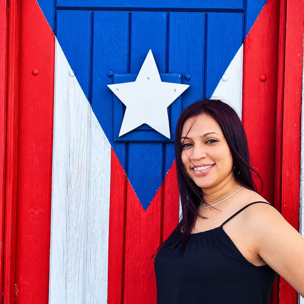 Lourdes M. Burgos Irizarry, creadora de Lú Designs, frente a una puerta decorada con los colores y la estrella de la bandera de Puerto Rico.