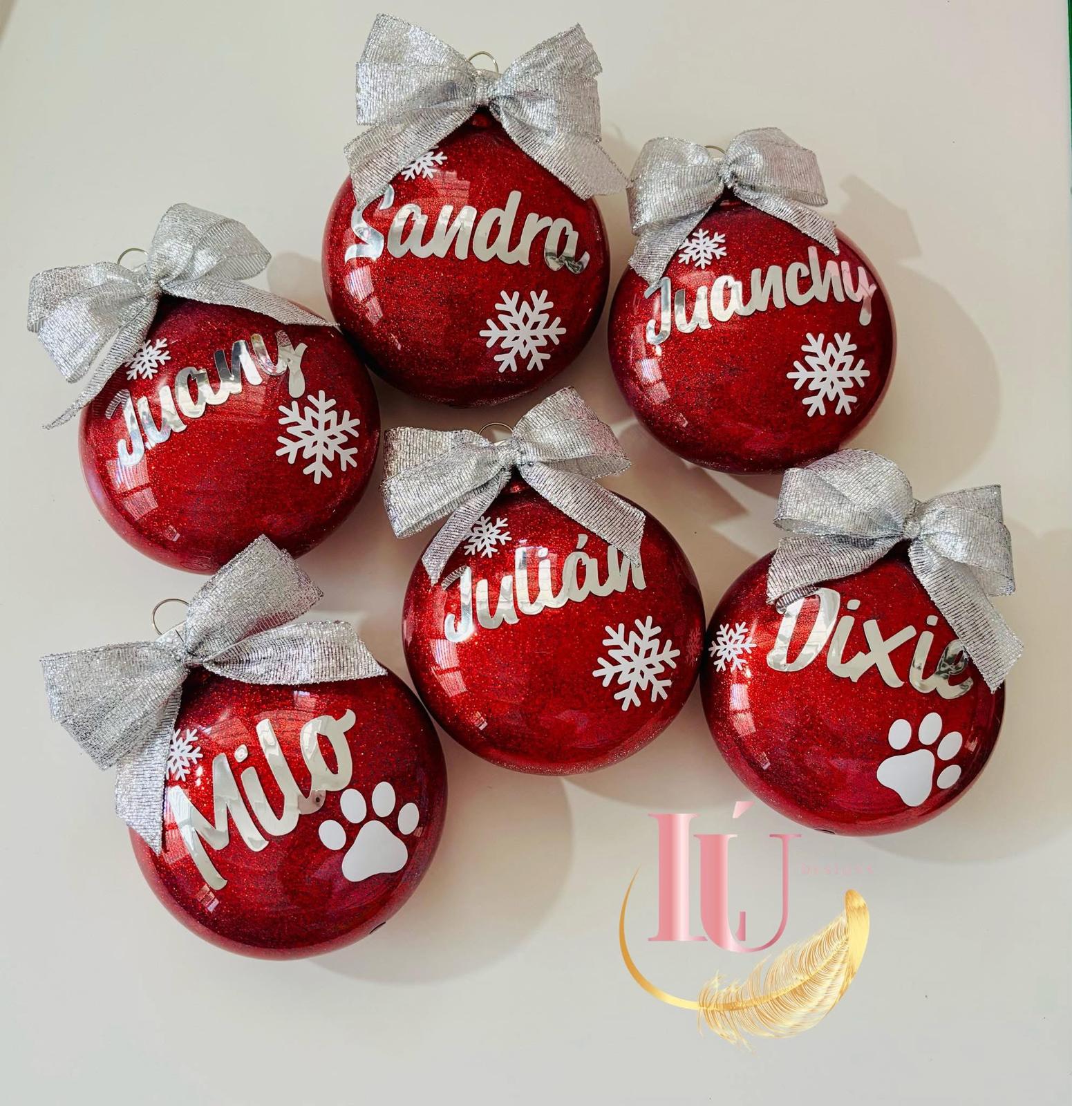 Bolas navideñas rojas personalizadas por Lú Designs con nombres, copos de nieve, lazos plateados y detalles decorativos.